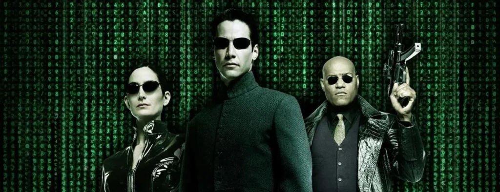 Trilogia Matrix - Onde assistir? Neo, Trinity e Morpheus vestindo roupas pretas e óculos escuros com as linhas da Matrix ao fundo.