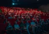 Cassinos no cinema: como Hollywood transformou as mesas de jogo em cenários inesquecíveis Plateia numerosa assistindo a sessão em cinema com poltronas vermelhas, iluminada pela luz da tela em ambiente escuro.
