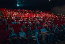 Cassinos no cinema: como Hollywood transformou as mesas de jogo em cenários inesquecíveis Plateia numerosa assistindo a sessão em cinema com poltronas vermelhas, iluminada pela luz da tela em ambiente escuro.